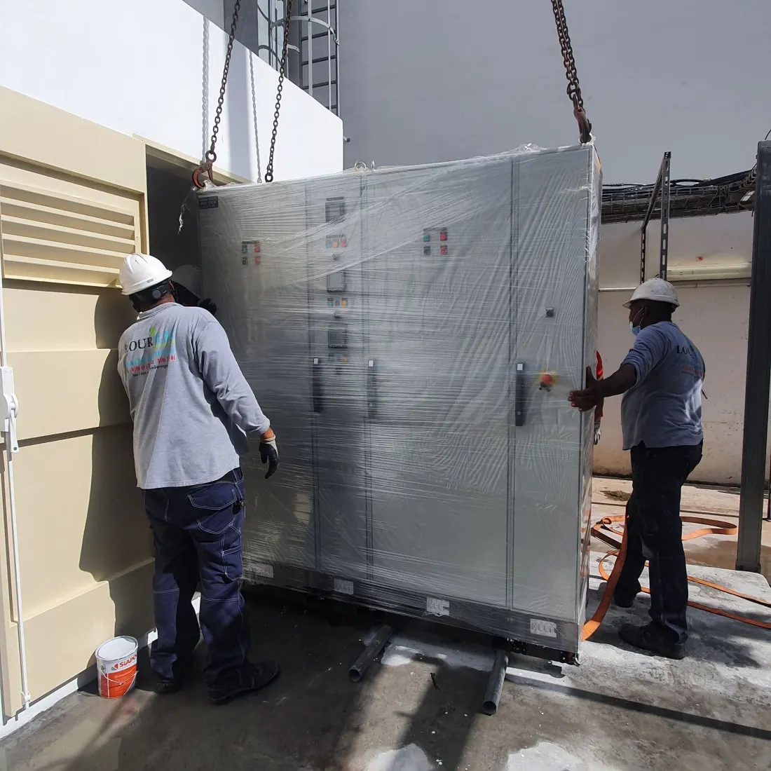 Deux techniciens Lourelec en casque de chantier positionnant une armoire électrique sur le site de la Cité Hospitalière Mangot Vulcin